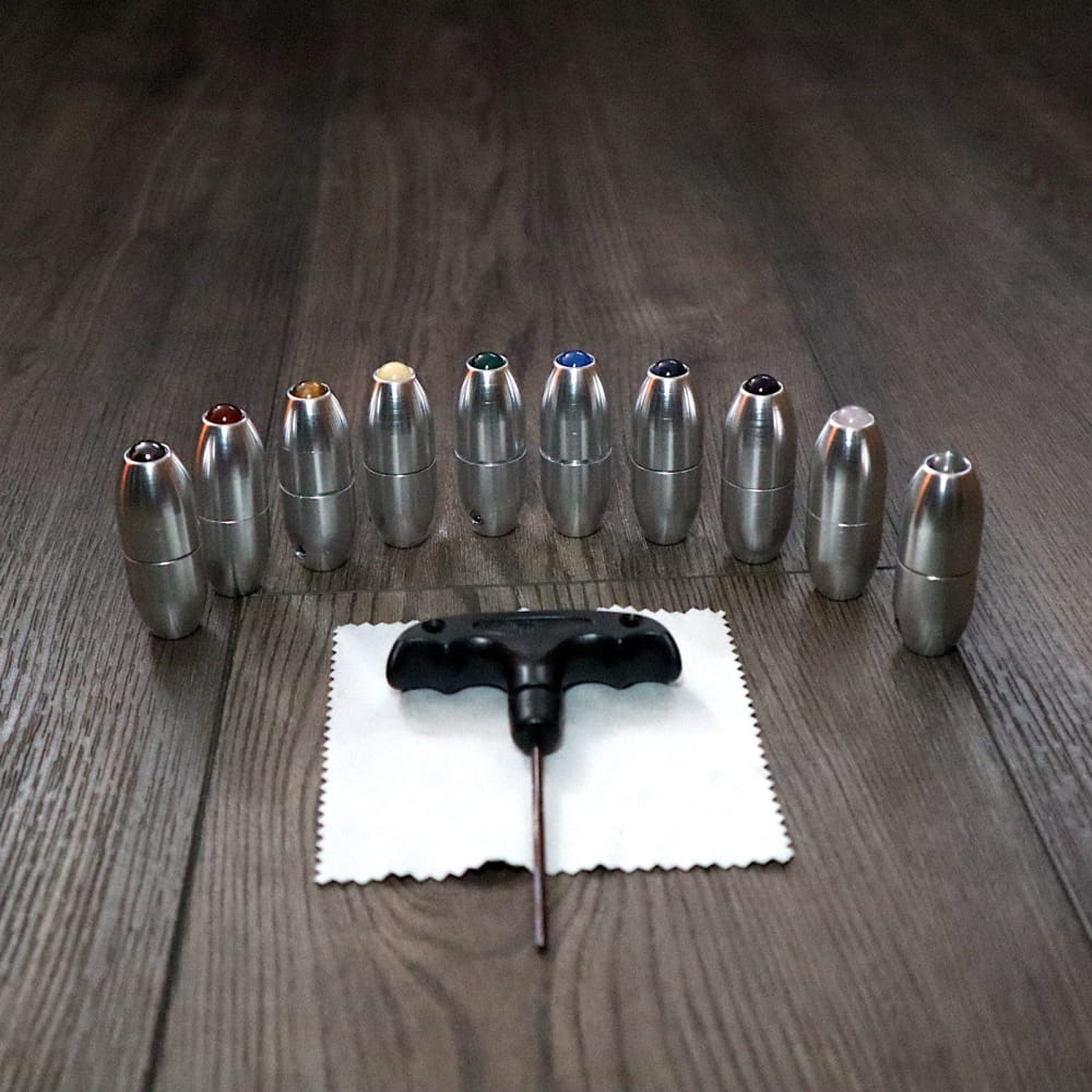 Metallic bullets in semicircle around black cross tool on white cloth with Crystal Tuning Fork Handles