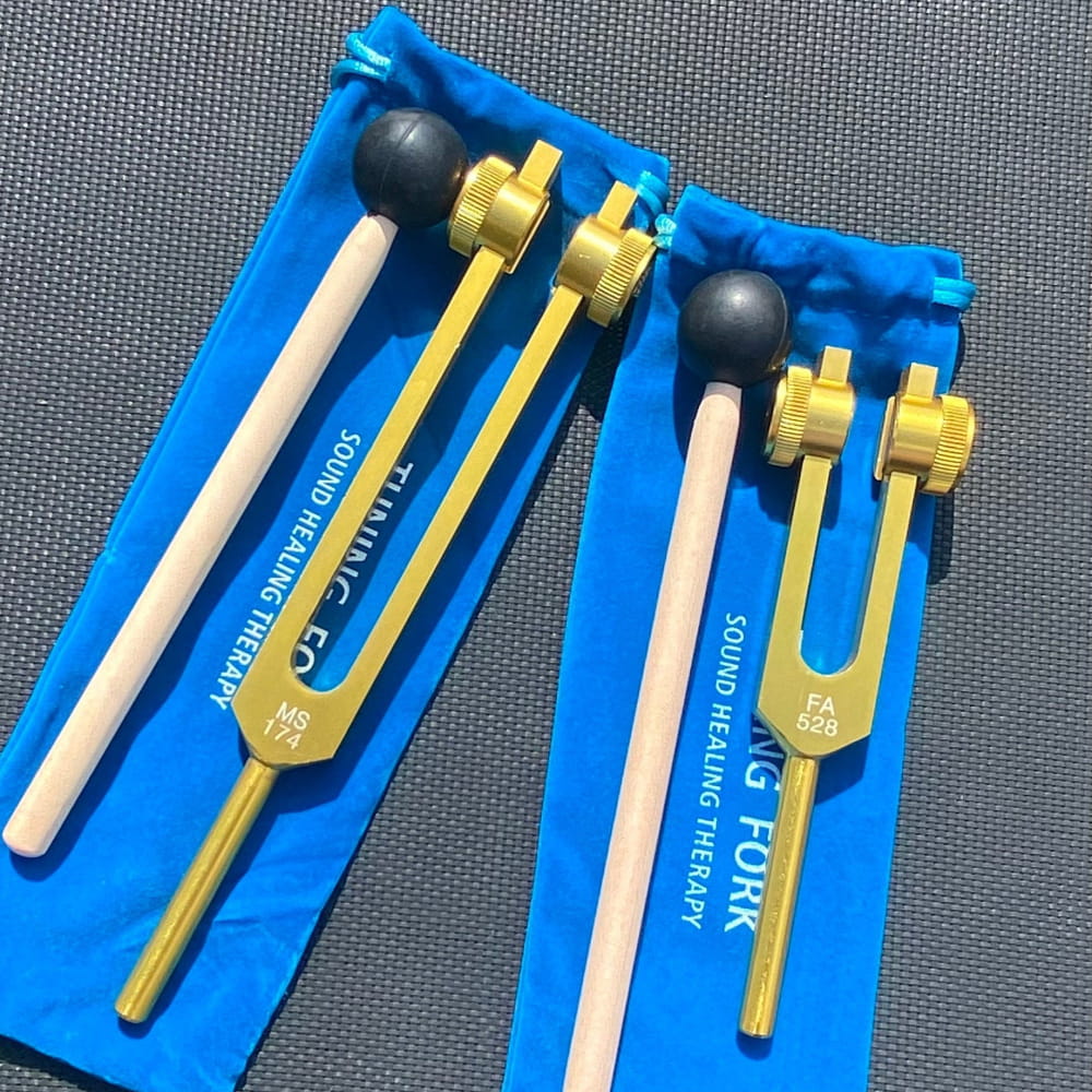 Two gold tuning forks with black mallets in blue sleeves for sound healing set