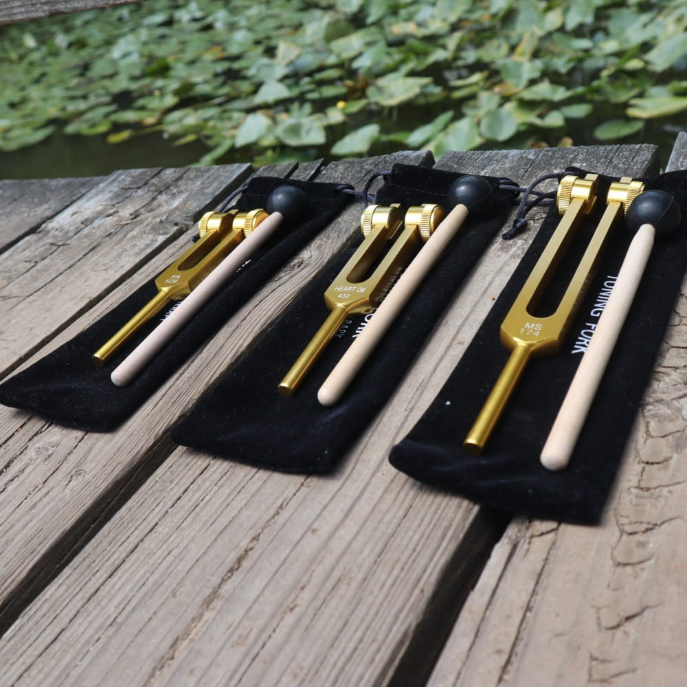Three gold tuning forks with white handles on black fabric for Solfeggio healing set