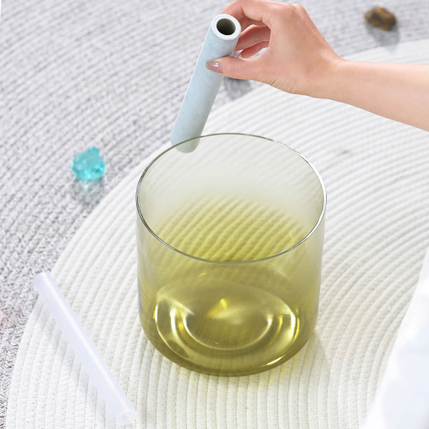 Glass container with yellow liquid stirred by light blue wand beside Quartz Crystal Singing Bowl
