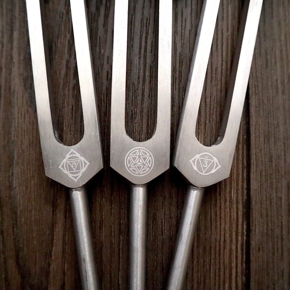 Three metal tuning forks with engraved chakra symbols for healing and balance