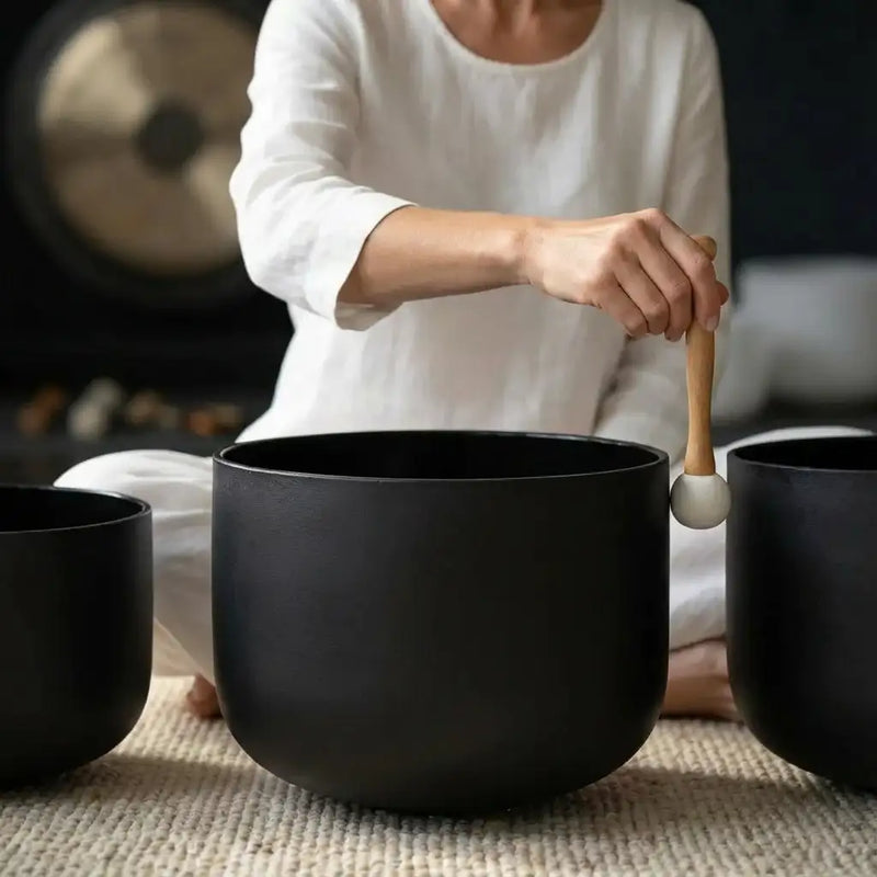 Black ceramic singing bowl with a wooden mallet featuring a white spherical head.
