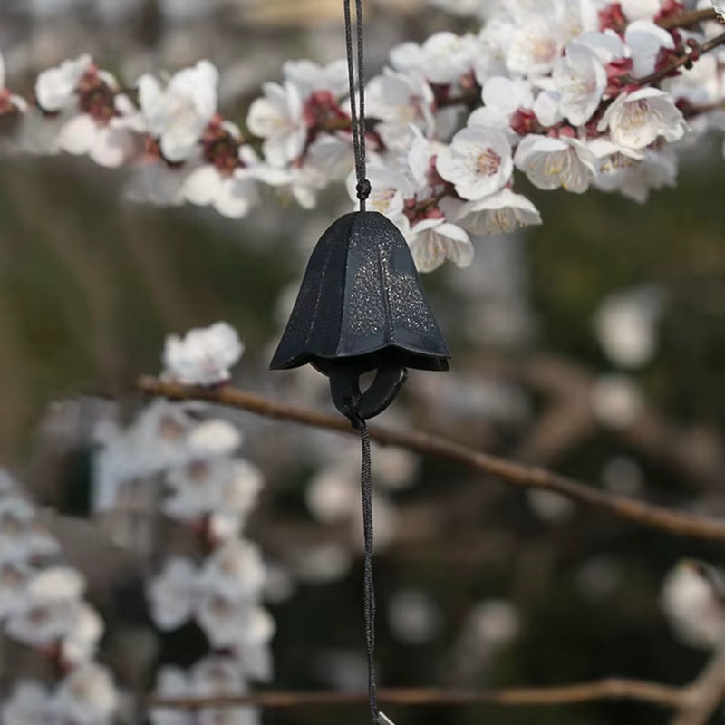 Dark bell-shaped iron wind chime surrounded by cherry blossoms for home and garden decor