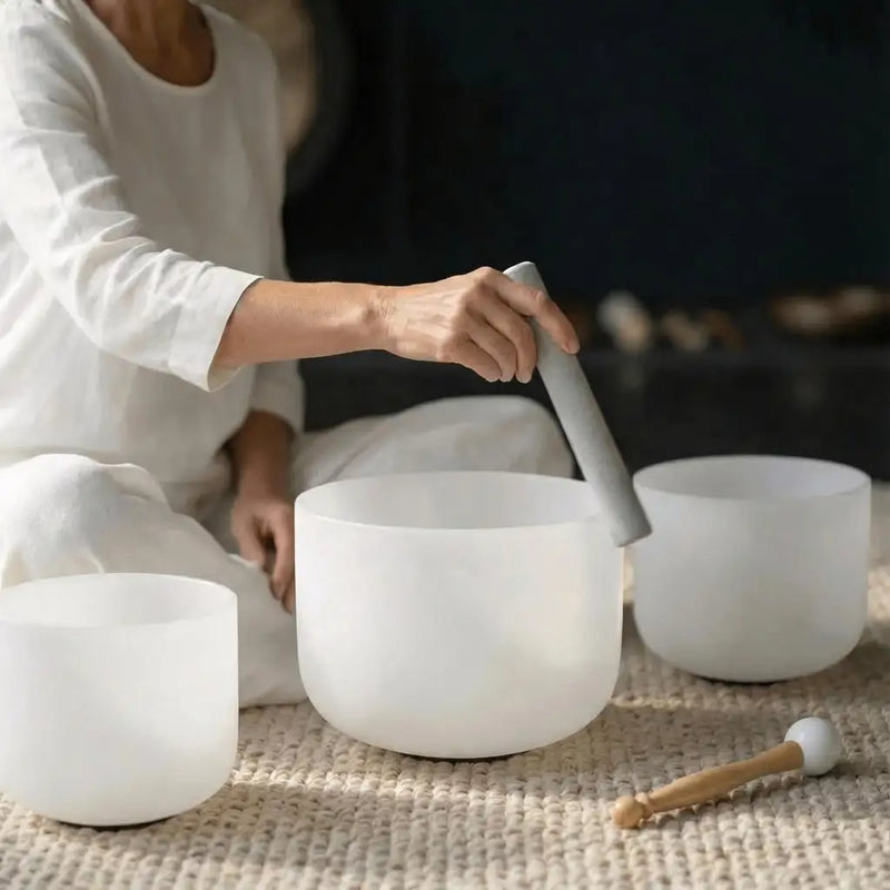 A set of three frosted white crystal singing bowls, one being struck by a matching mallet.