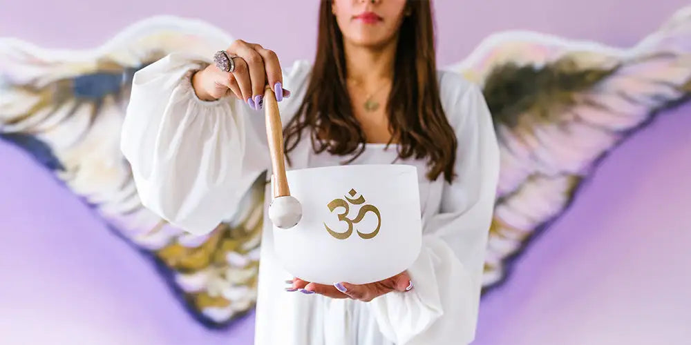 White ceramic singing bowl with a gold om symbol etched on its surface, held by a person in a white robe.