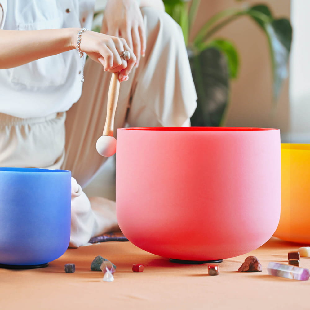 Pink crystal singing bowl with blue and orange bowls and scattered crystals