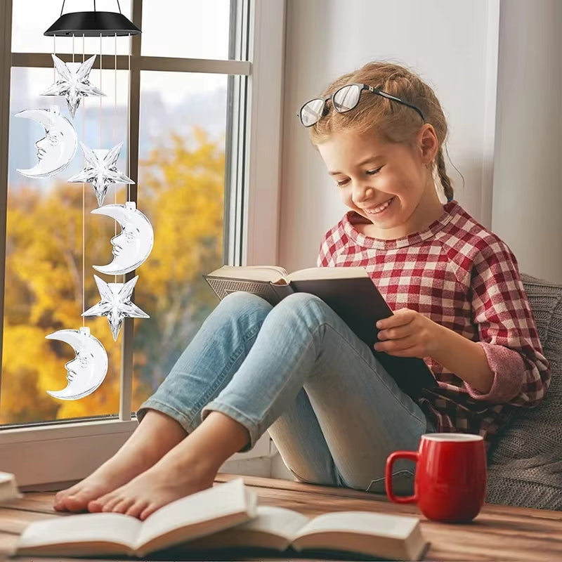 Reader enjoying a book by a window with Solar Butterfly Wind Chimes glowing nearby