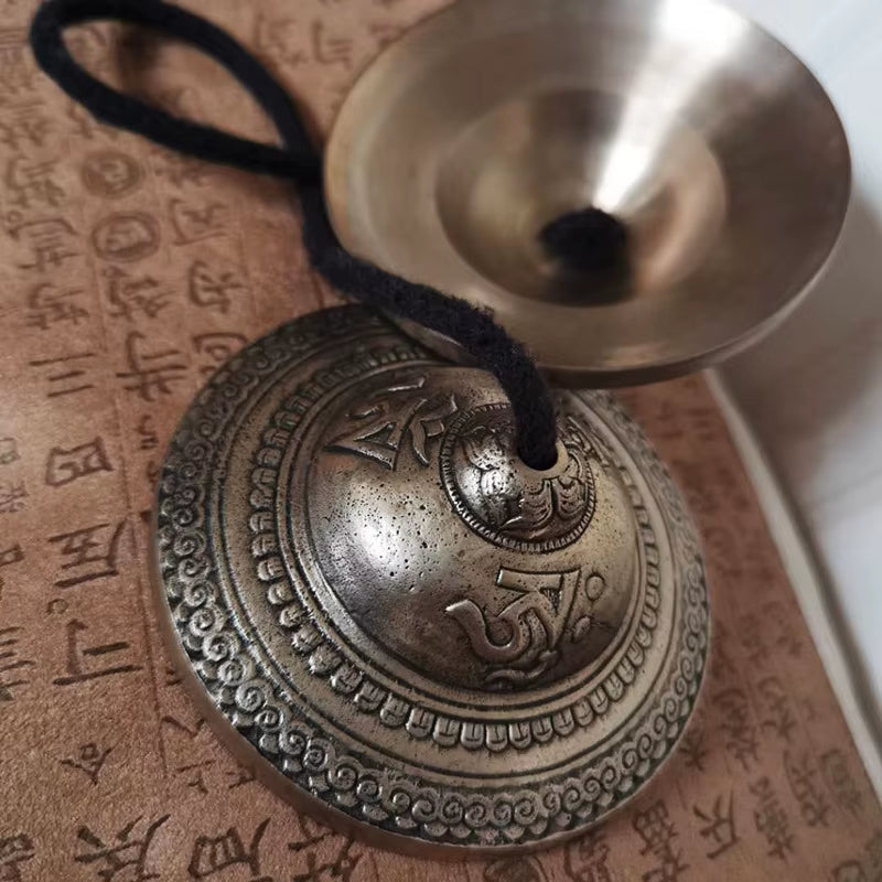 Metallic Tibetan meditation bell with ornate patterns and black cord for sound healing